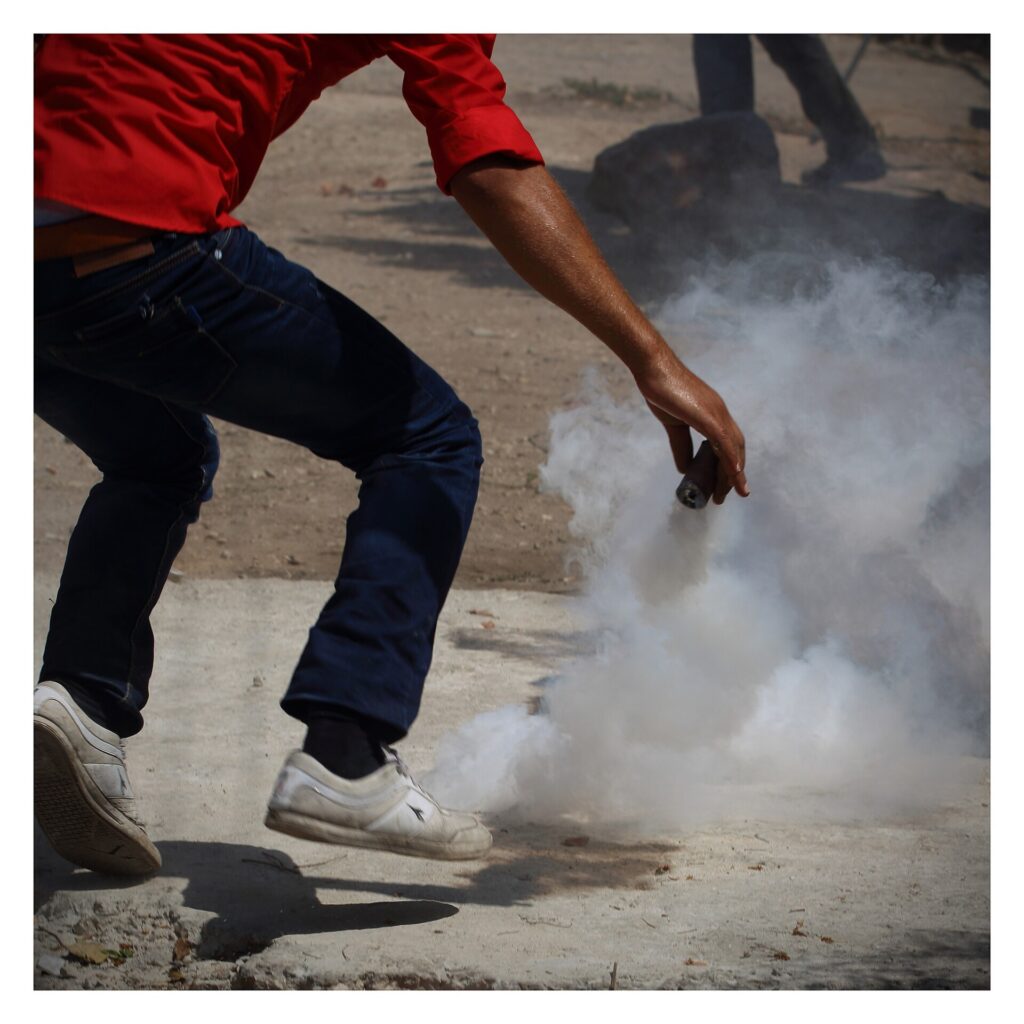 Palestinian Demonstrator picks Tear gas grenade to throw back Kafr Qaddum August 2014 2.jpg